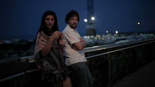 Couple discussing at night on bridge in front of port and ocean