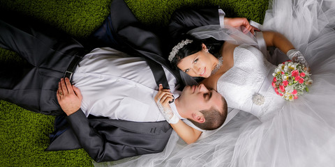 Smiling bride and groom lying on the grass-like carpet.