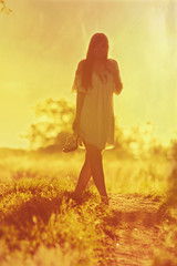 Young girl goes barefoot on a dirt road in a field at sunset. Instagram toned.