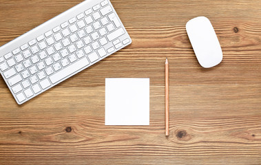 Top view office workplace - blank white notepad, pencil, keyboard and mouse on dark wooden background with copy space