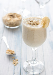 Healthy banana smoothies with oatmeal in a glass on a blue background