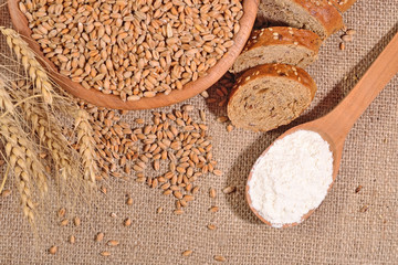 White flour in a wooden spoon, wheat and bread