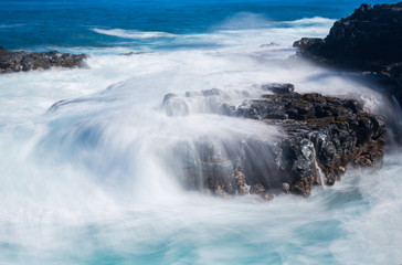 Raging sea flows over lave rocks on shore line