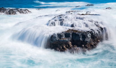 Raging sea flows over lave rocks on shore line