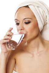 woman with a towel on her head drinking water from a glass 