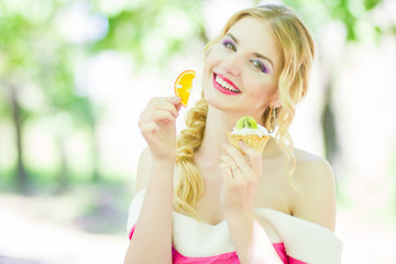 Portrait of a beautiful young blonde woman with long hair on nature. A girl holding a cake with fruit. Soft focus