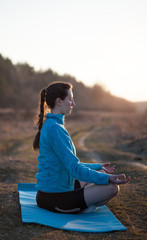 Brunette woman practicing yoga outside during sunset wearing sports wear with eyes closed