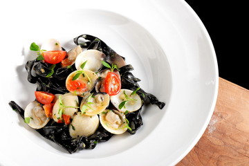 Close-up of squid ink colored tagliatelle with sliced octopus and vongole mussels