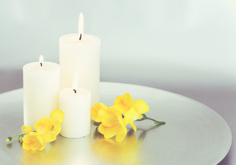Fototapeta na wymiar Candles and yellow Freesia blossoms with silver background. 