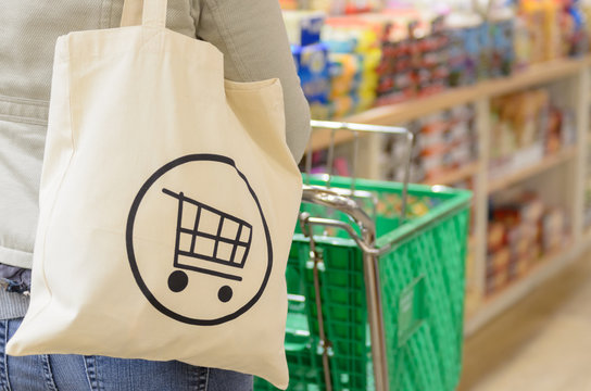 Close up of a female shopper with a canvas tote bag pushing a shopping cart down the isle of a specialty grocery store.