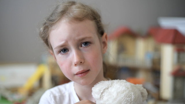 Crying little girl with bear in the children's room.
