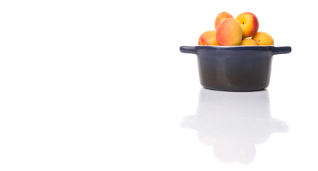 Ripe apricot fruits in a bliue pot over white background