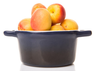 Ripe apricot fruits in a bliue pot over white background