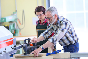 Carpenter showing apprentice how to use sawing machine