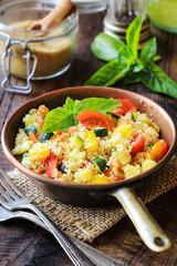 Delicious homemade gluten free vegetarian couscous with tomatoes, carrots, zucchini, yellow bell pepper and fresh basil on a dark rustic wooden kitchen table