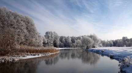 Fototapeta premium Winter landscape with frosted river and white snow. Small river, surrounded by snow-covered trees and a beautiful sky with clouds