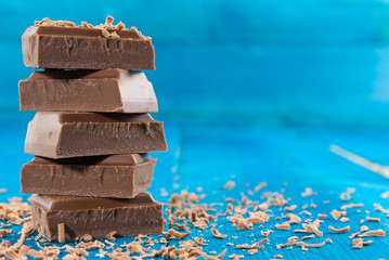 Closeup of roughly cut chunks of a chocolate bar and chocolate shavings on blue wooden background