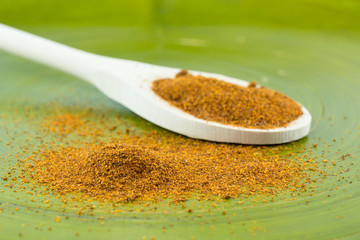 Red chili powder on wooden spoon and green background