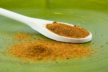 Red chili powder on wooden spoon and green background