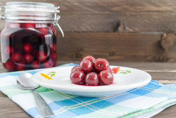 Vintage look of sour cherries on spoon and in the background the jar with sour cherry compote