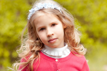 Beautiful child 4-5 year old girl posing over green nature background. Looking at camera. Wearing floral hairband. 