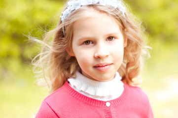 Smiling blonde kid girl 10-12 year old looking at camera. Posing outdoors over nature background 