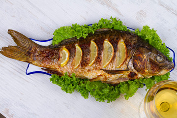 Whole grilled fish carp served with salad and lemon; glass of wine