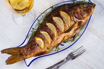 Whole grilled fish carp served with salad and lemon; glass of wine