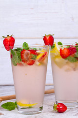 Lemonade with fresh strawberries mint and lemon on wooden background