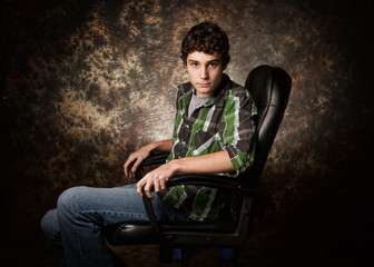 Fototapeta na wymiar teen boy sitting in a chair looking serious