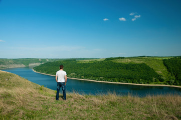 Naklejka premium Young man stands on the top of the hill viewing wide Dnister river