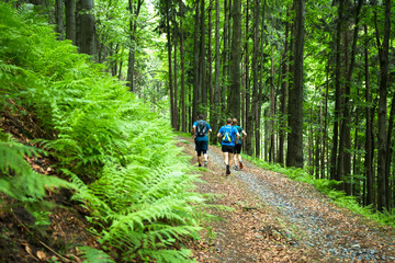 four men running together on the trail in the green forest 