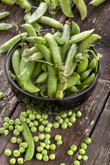.peas in pods in black bowl on a wooden table