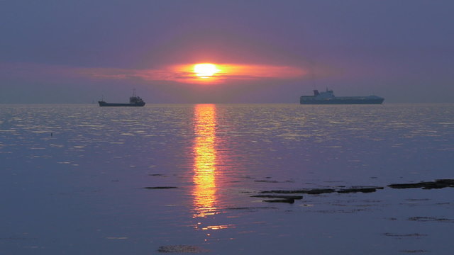 Boats navigating on sea horizon at sunset with sun reflections on water