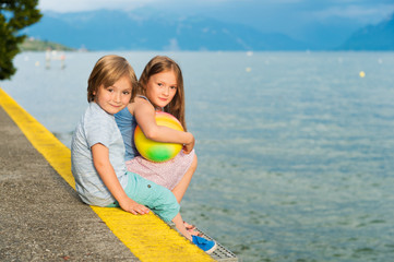Fototapeta premium Two cute kids resting by the lake at sunset