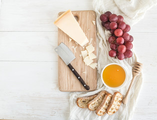 Parmesan cheese with grapes, honey and bread slices on wooden