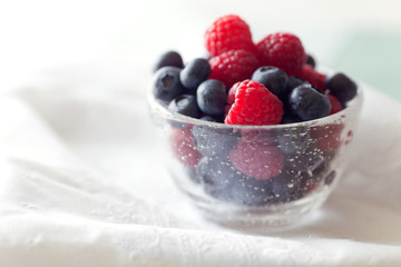 Fresh Berries, blueberries and raspberries in a blown glass bowl on eyelet lace linens. 