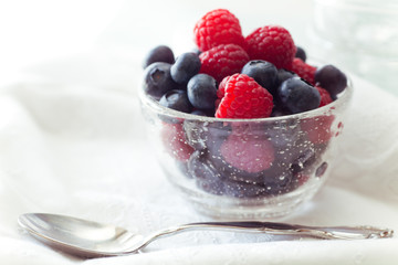 Fresh Berries, blueberries and raspberries in glass bowl with spoon. 