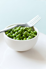 Freshly shelled green peas in a white bowl with fork. 