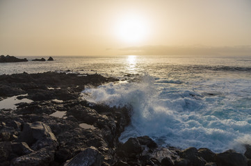 Sun setting over waves breaking on seacoast of Tenerife island,