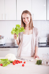 smiling young woman standing in kitchen , holding bright green s