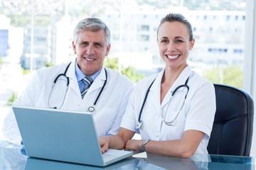 Smiling doctors working together on laptop