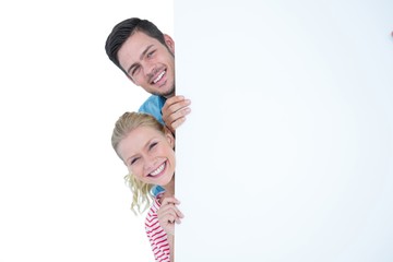 Smiling young couple hiding behind a blank sign