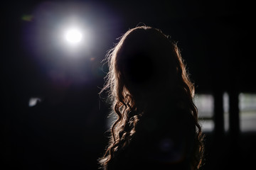 Dunkelheit / Eine Frau steht in einem dunklen Raum und wird von einem Scheinwerfer von hinten angeleuchtet. Zu sehen ist nur ihre Silhouette.