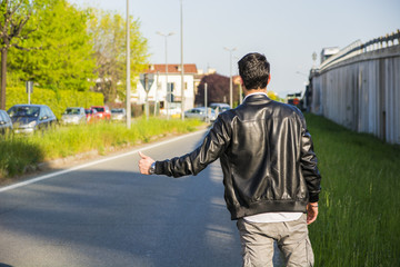 Back of young man, hitchhiker waiting on roadside