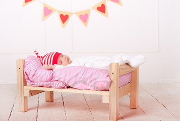 Cute baby lying in bed with valentines hearts on background