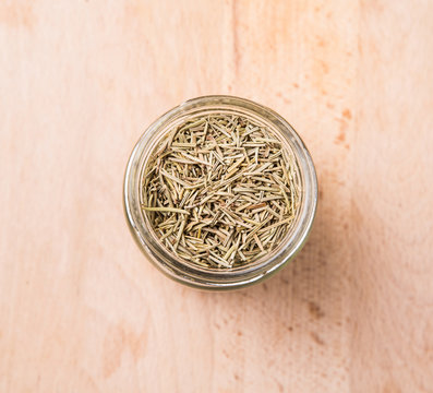 Dried rosemary herb leaves in a mason jar on wooden board