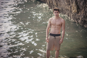 Young shirtless athletic man standing on rock by sea