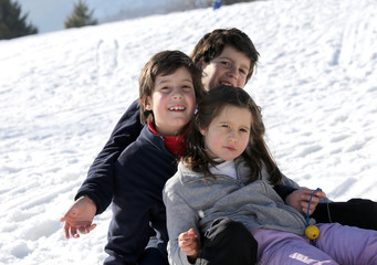 Fototapeta na wymiar three smiling siblings over the sled in winter in the mountains