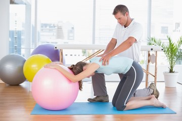 Trainer working with woman on exercise ball